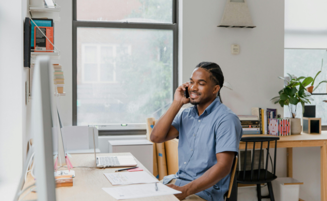 Man setting at a desk smiles while talking on a cell phone