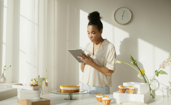 Woman holds a tablet while standing by a table with desserts on it